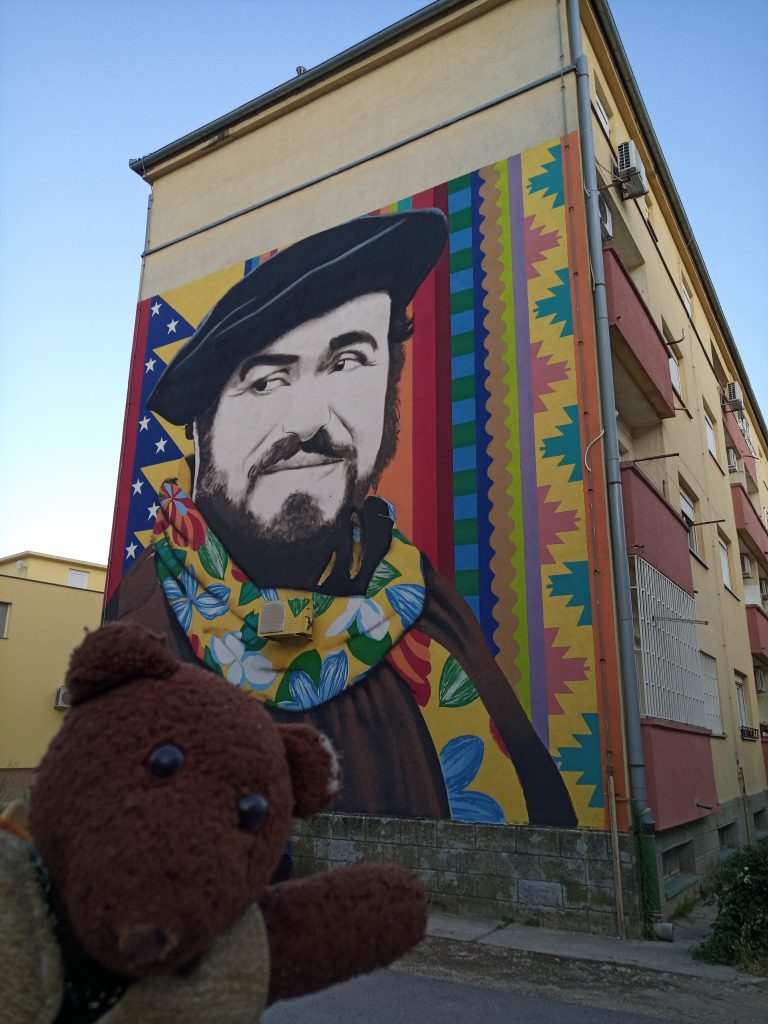 Bearsac in foreground of block of flats with Pavarotti painted on the side
