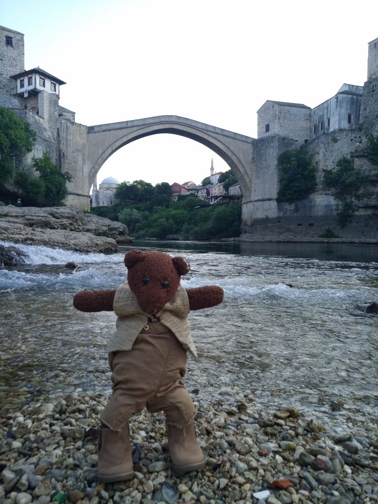Bearsaxc standing on river stones in foreground of the famous bridge in Mostar
