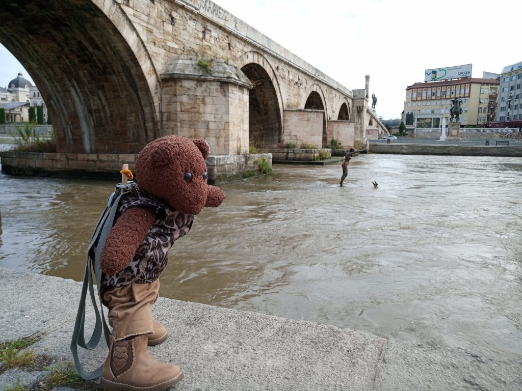 Bearsac standing beside a stone bridge and river