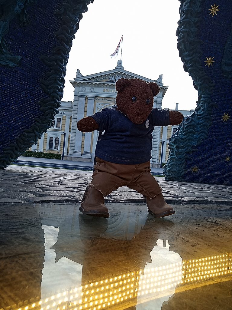 Bearsac standing underneath a monument witha flagged building in the background