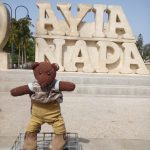 Bearsac the teddy bear in the forground of the worded Aya Napa monument