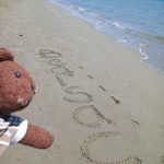 Bearsac te teddy bear with his name in the sand.
