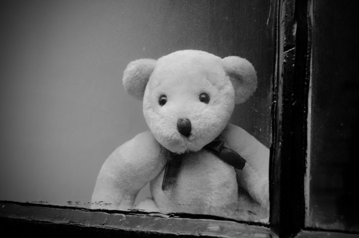 Sad looking teddy bear looking out from behind a window