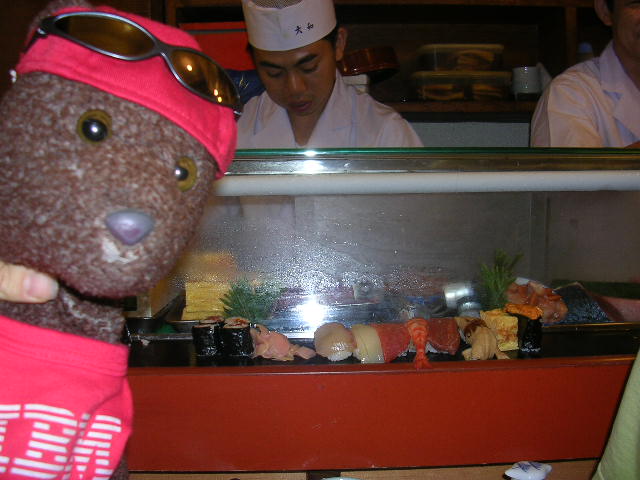 Bearsac beside fish topped sushi on cold bar.