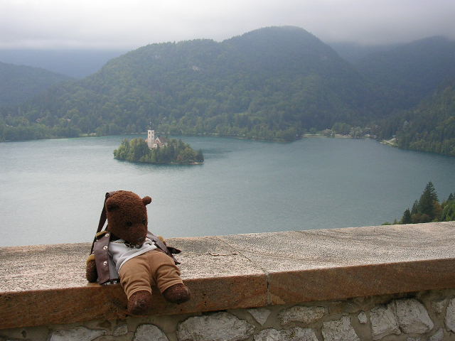 Bearsac sitting a wall with Lake Bled and Church of the Assumption behind.