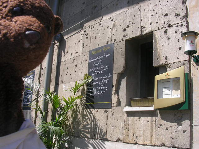 Bearsac beside building with many bullet holes