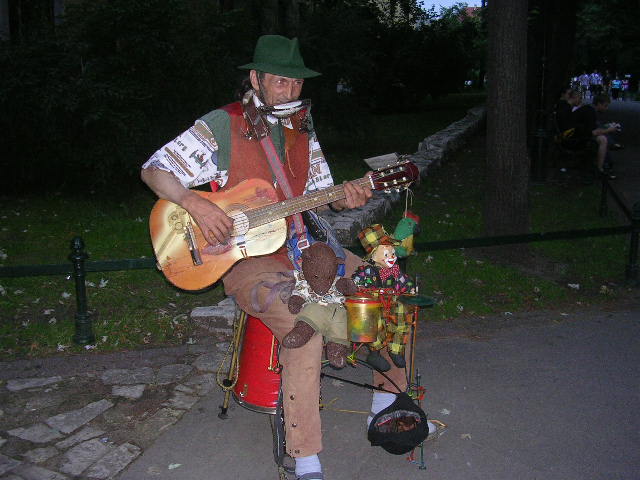 Bearsac sitting of the knee of a one-man-band busker with a clown puppet