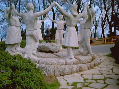 Bearsac sitting in the middle of a ring of statute dancers holding raised hands