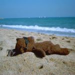 Bearsac lying on the beach, naked apart from sunglasses.