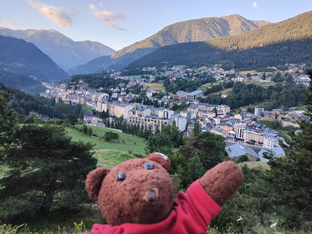 Teddy bear Bearsac in the foreground of a mountain view with the city in the valley.