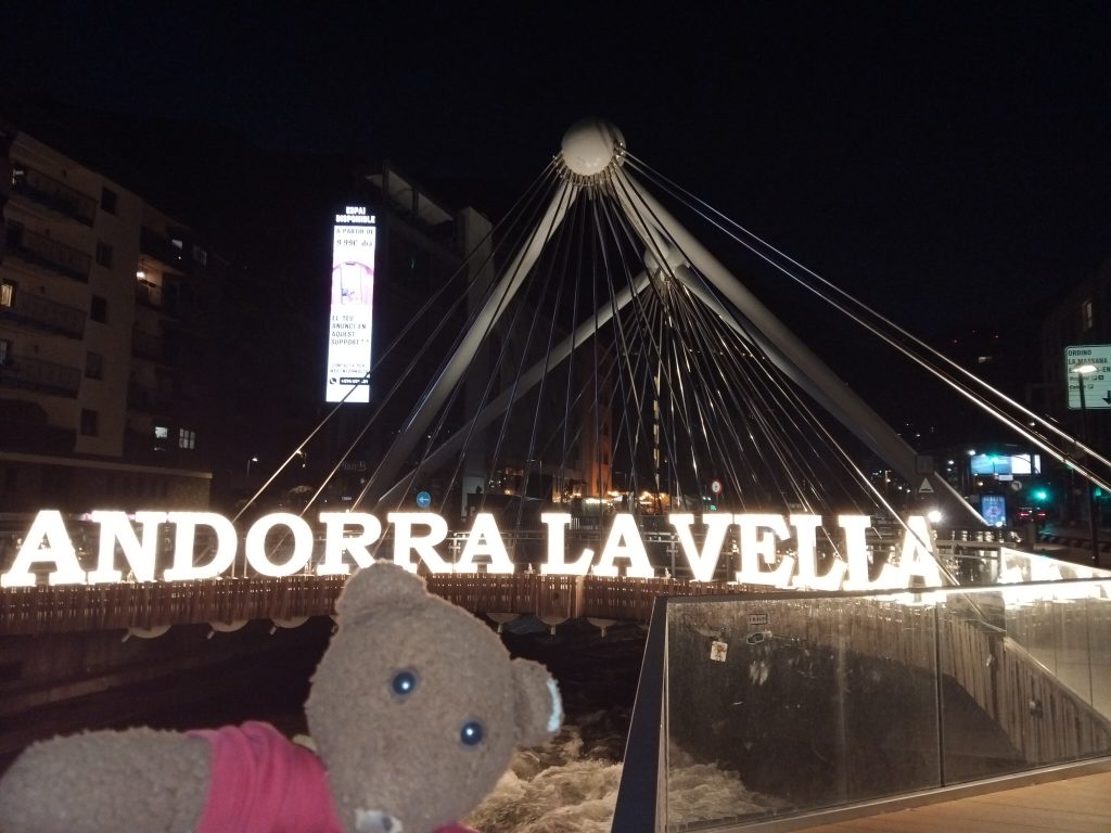Teddy bear Bearsac in the foreground of Pont de París, with the wording Andora La Vella kit up.
