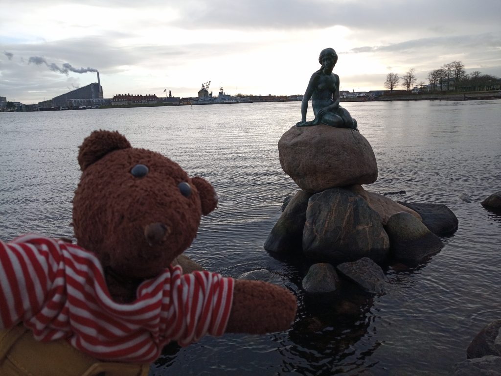 Teddy bear Bearsac in the foreground of The LIttle Mermaid statue