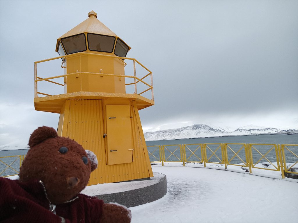 Teddy bear Bearsac in forground ofa yellow lighthouse