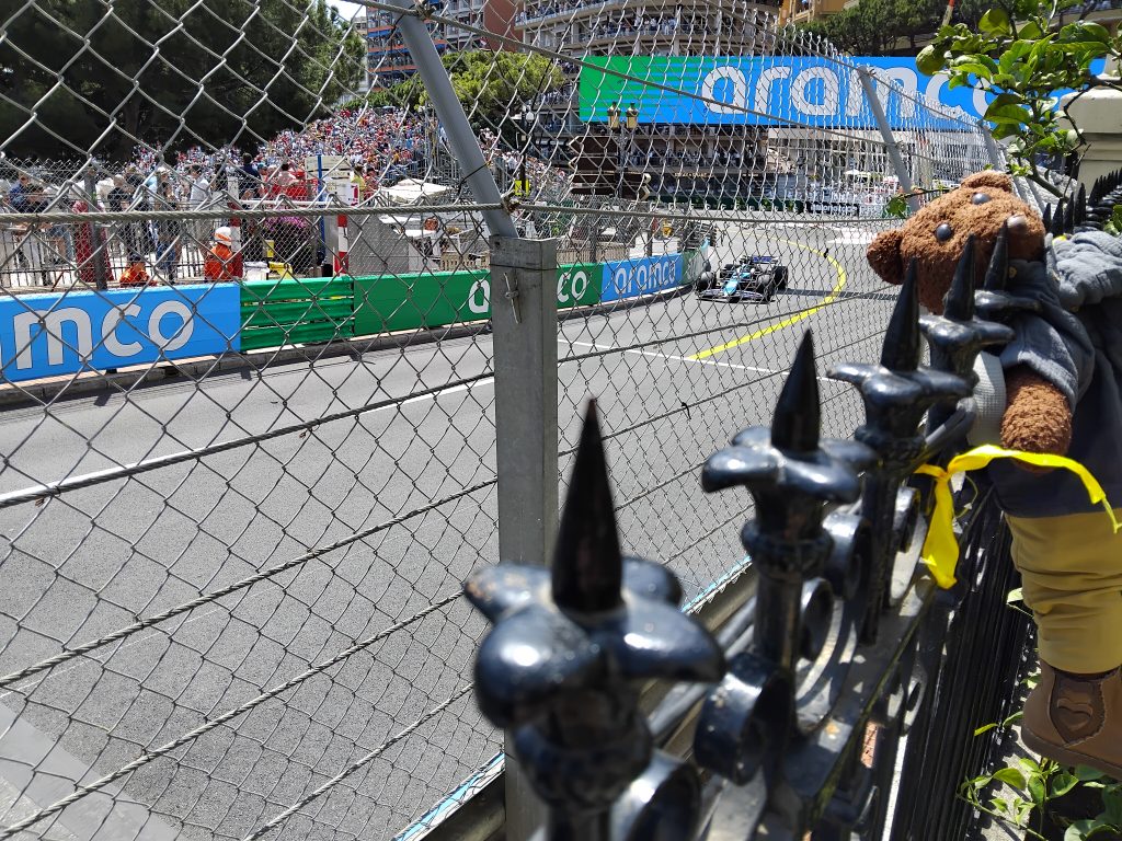 Teddy bear Bearsac om a fence in the foreground of the GP race track.