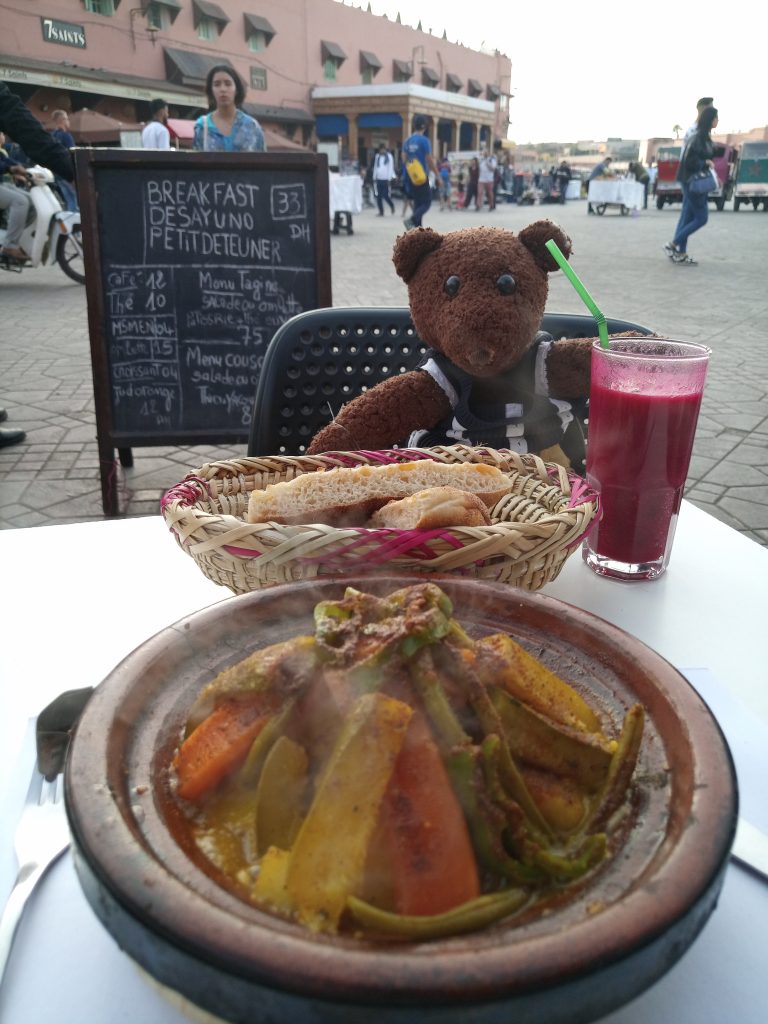 Teddy bear Bearsac sitting a a table with a steaming vegetable tangine