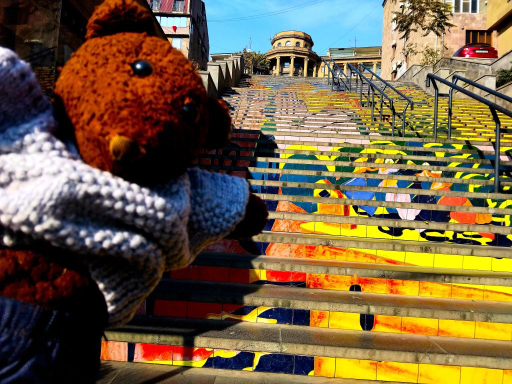 Bearsac the teddy bear in forground of coloufully painted steps.