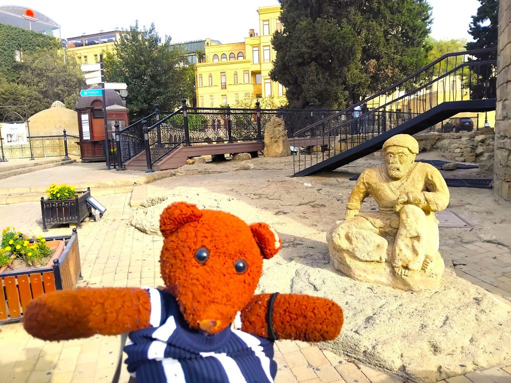 Bearsac the teddy bear in forground of a statue