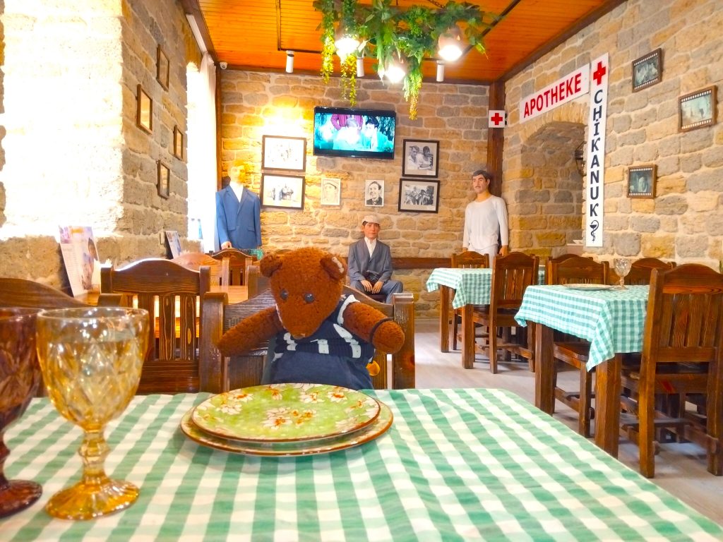 Bearsac the tddy bear sitting at atable with food.