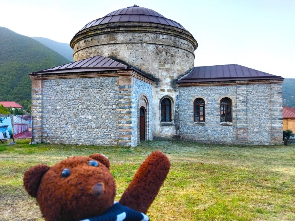 Bearsac the teddy bear in forground of Nukha Three Saints church.