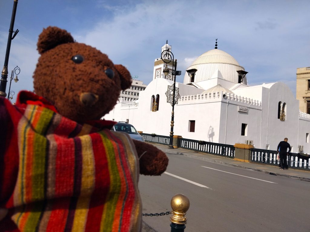 Bearsac the teddy bear in forground of a mosque