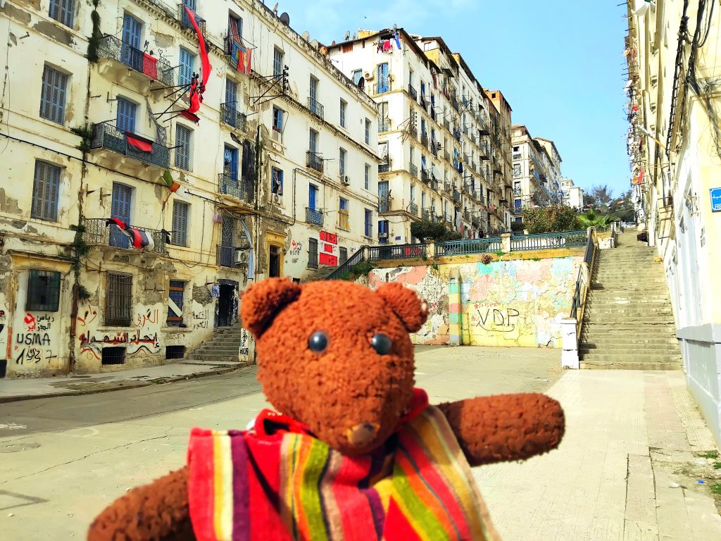 Bearsac the teddy bear in forground of backstreet buildings