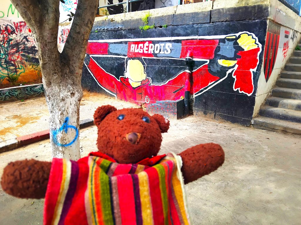 Bearsac the teddy bear in forground of wall art.