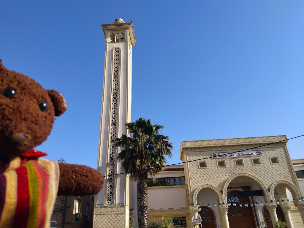 Bearsac the teddy bear in forground of a mosque