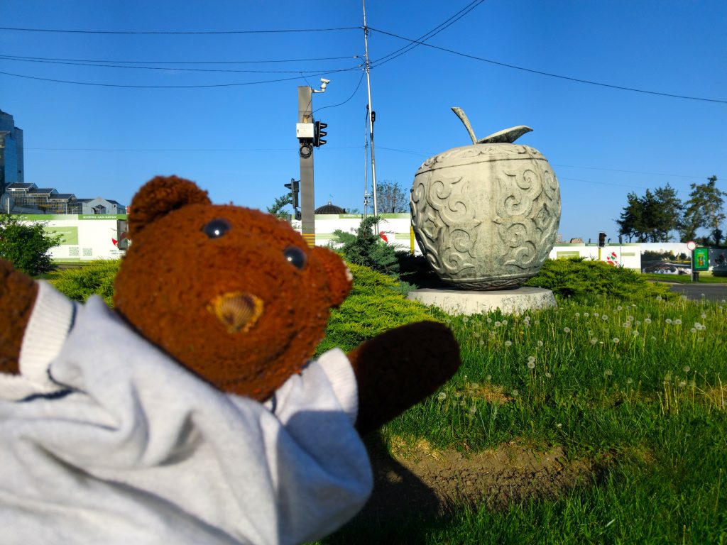 Bearsac the teddy bear in the forerground of the apple monument