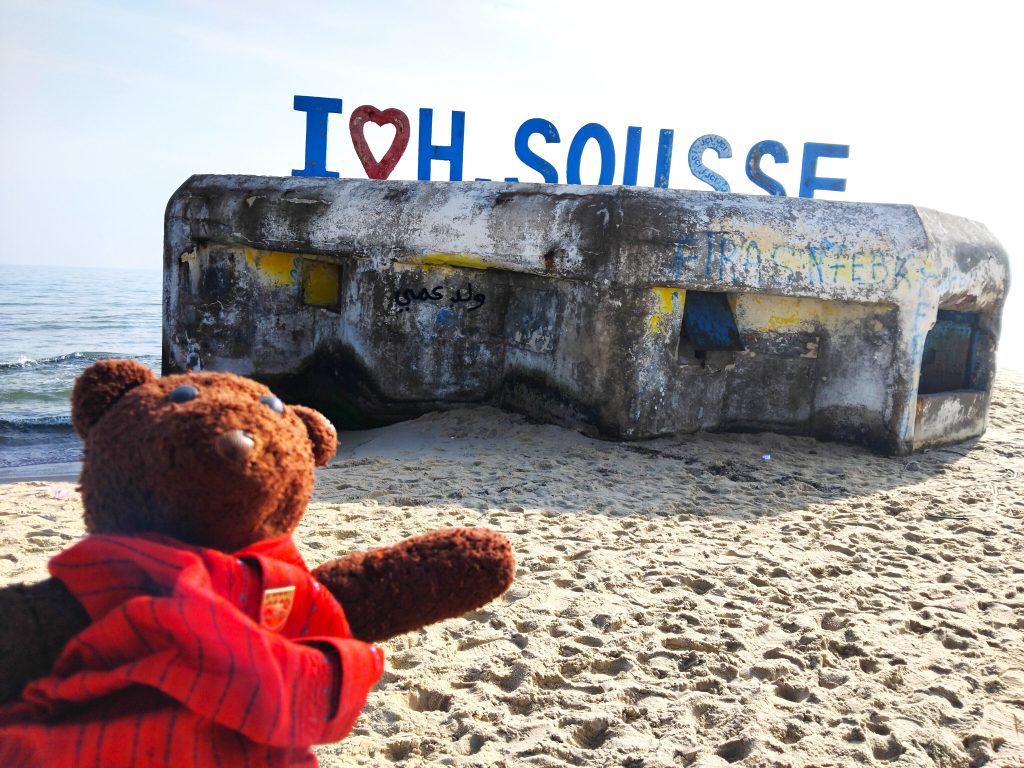 Bearsac the teddy bear in the forground of I love Sousse sign on top of an old war pil box.