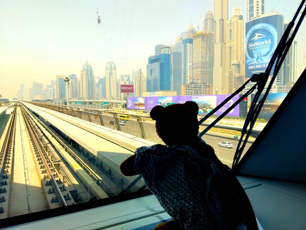 Bearsac the teddy bear sitting on a ledge att he front of the metro train