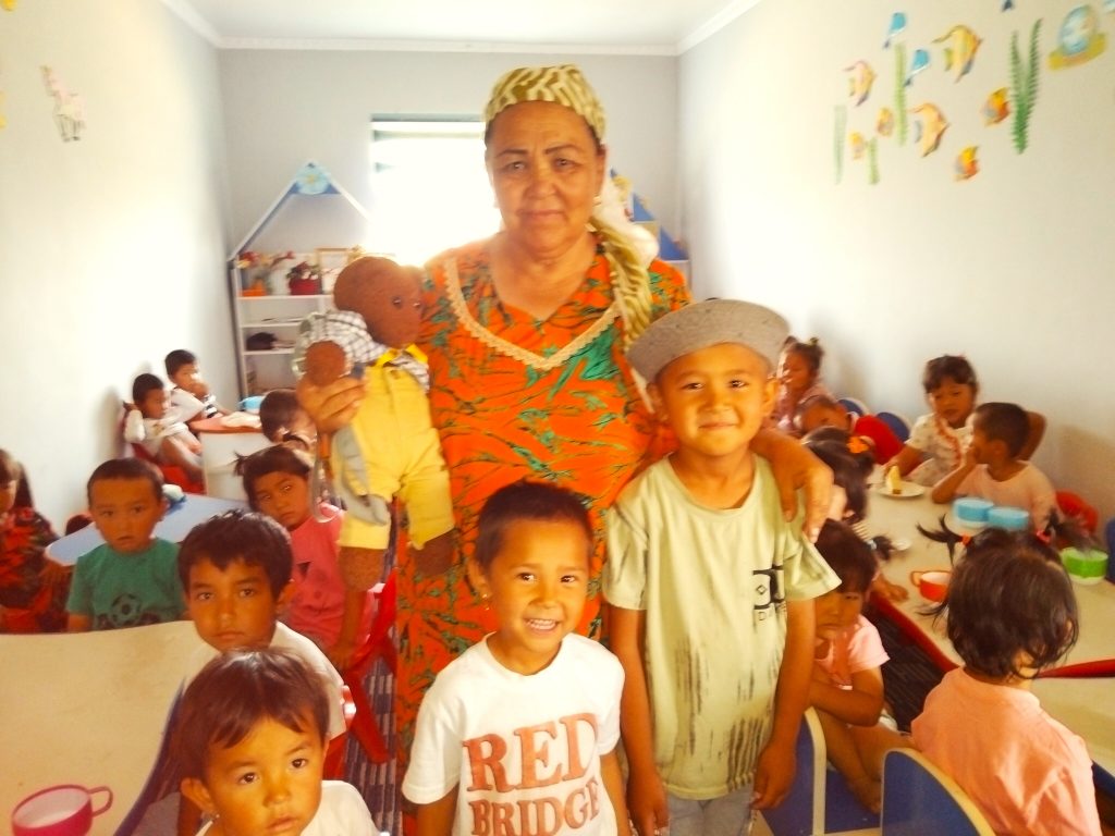 Bearsac the teddy bear being held by a women standing with children.