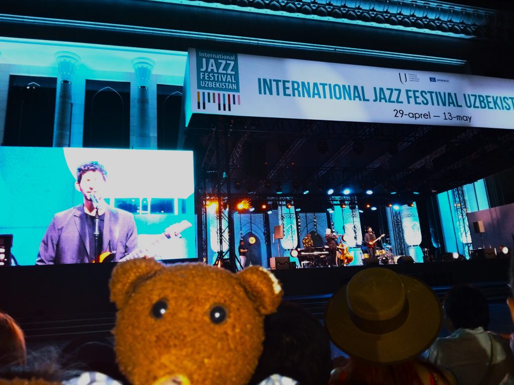 Bearsac the teddy bear in the foreground of an outside stage.