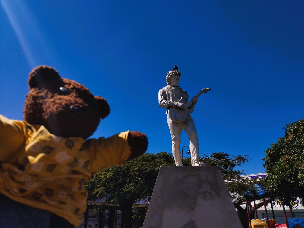 Bearsac the teddy bear in foreground of a monument of a rock star