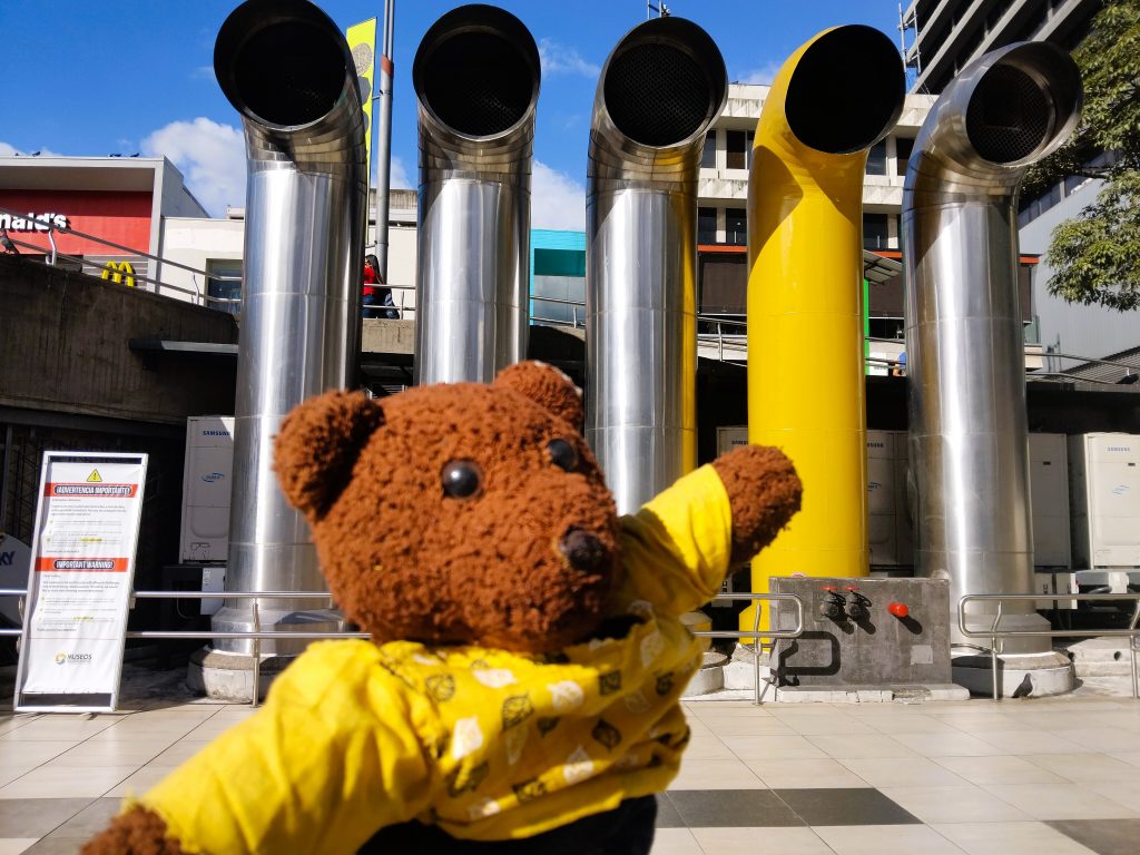 Bearsac the teddy bear in foreground of 5 air funnlels. One the same yellow as his top.