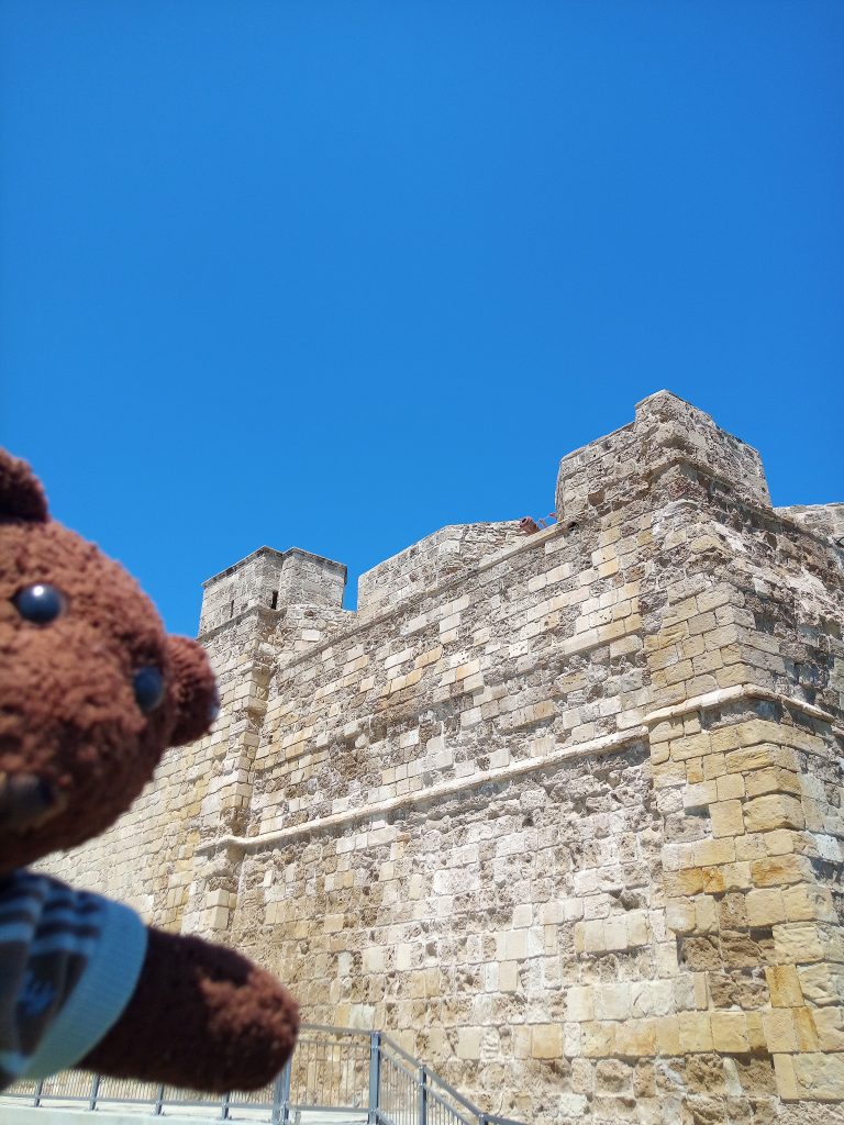 Bearsac the teddy bear in forground of Larnaca Castle