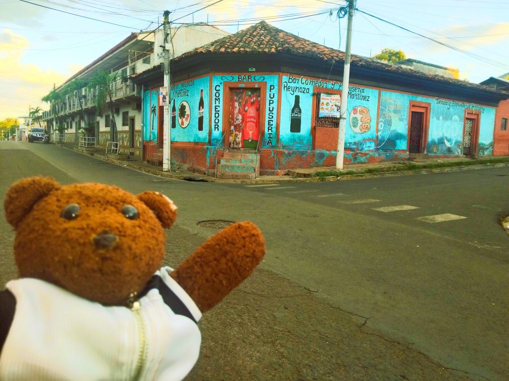 Bearsac the teddy bear in foreground of a brightly coloured shop.