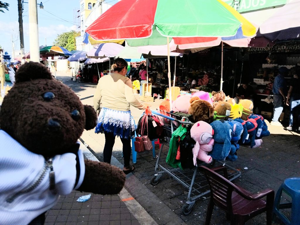 Bearsac the teddy bear in foreground of cuddly toys ina supermarket trolley at a street market.