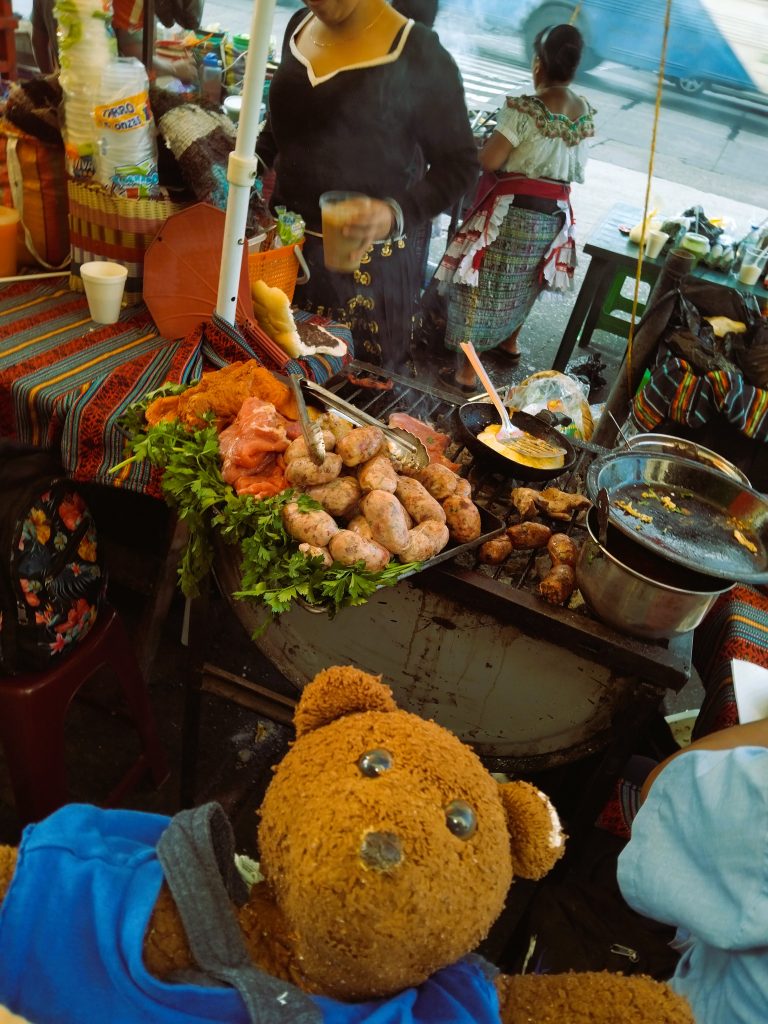 Bearsac the teddy bear in foreground of a street food stand.