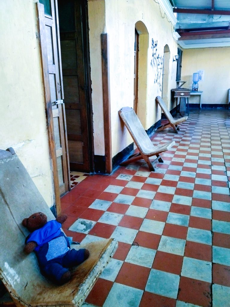 Bearsac the teddy bear sitting on a worn out chair in the corridor of a pension.