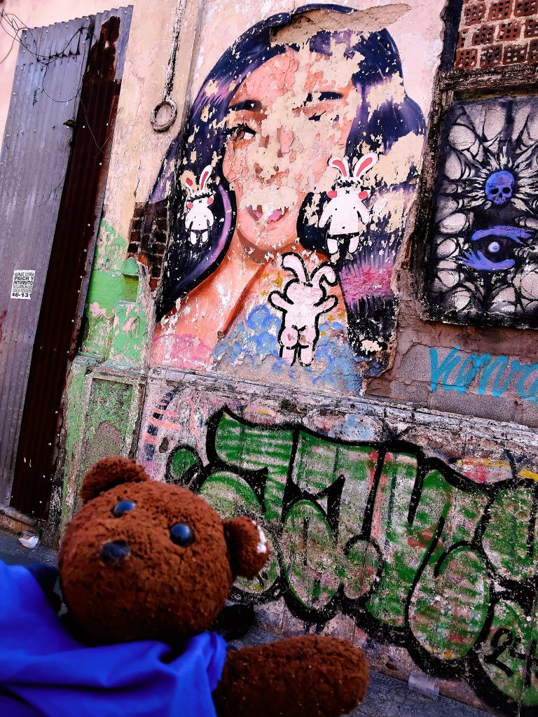 Bearsac the teddy bear in foreground of graffitti.