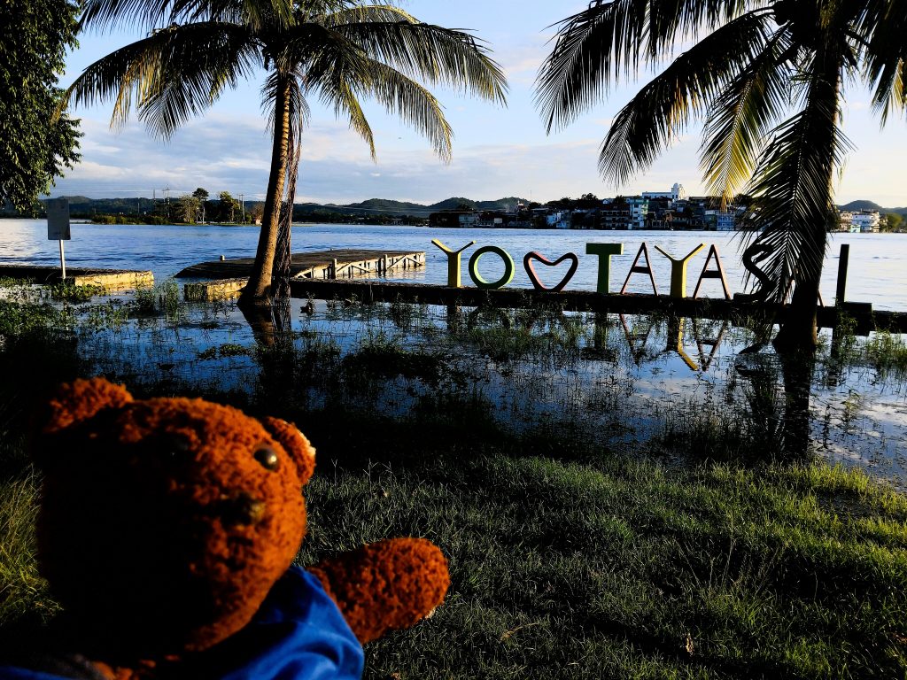 Bearsac the teddy bear in foreground of I Love Tayasal sign