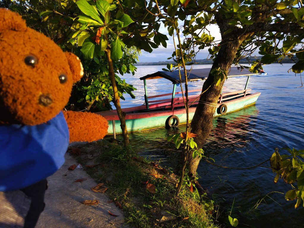 Bearsac the teddy bear in foreground of a moored boat and lake.