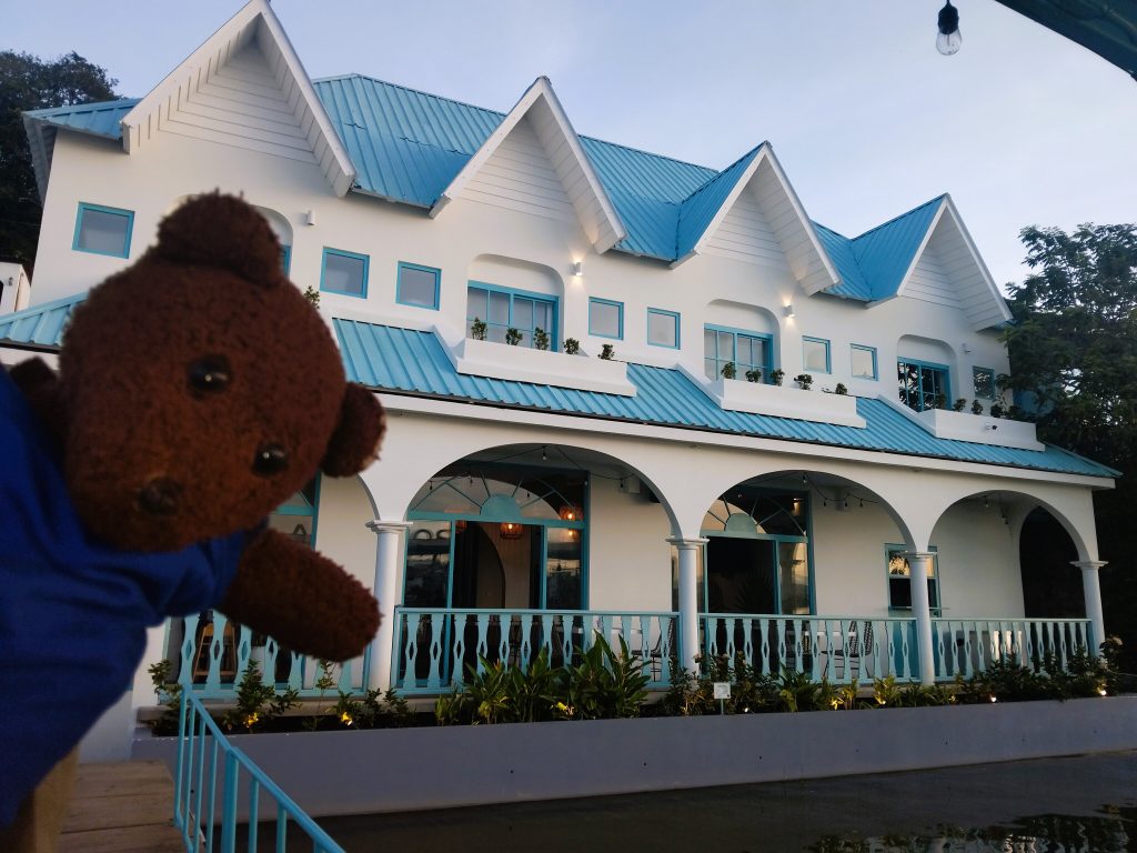 Bearsac the teddy bear in foreground of a blue and white hostel building.