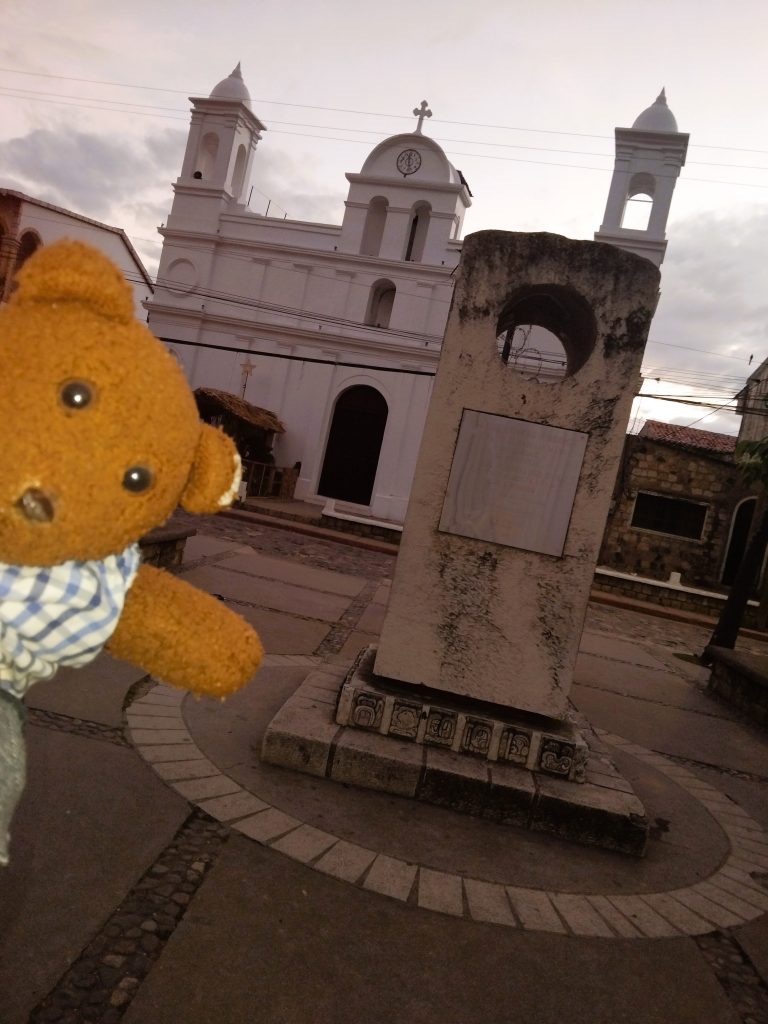 Bearsac the teddy bear in foreground of a church and monument.
