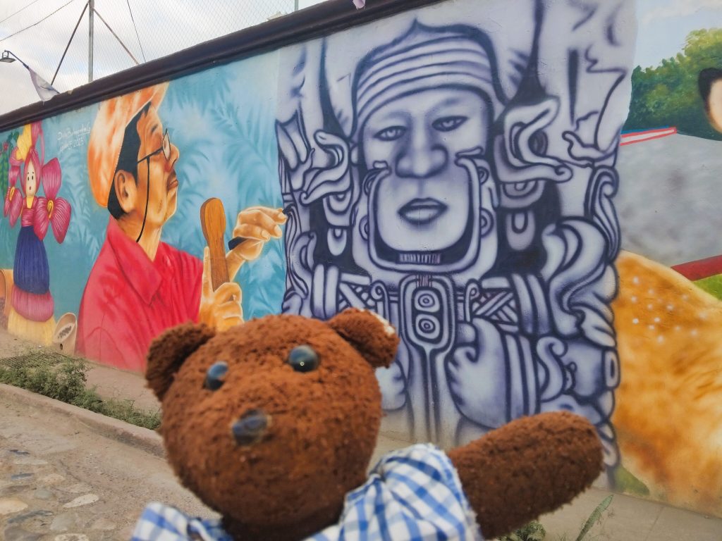 Bearsac the teddy bear in foreground of a murial.