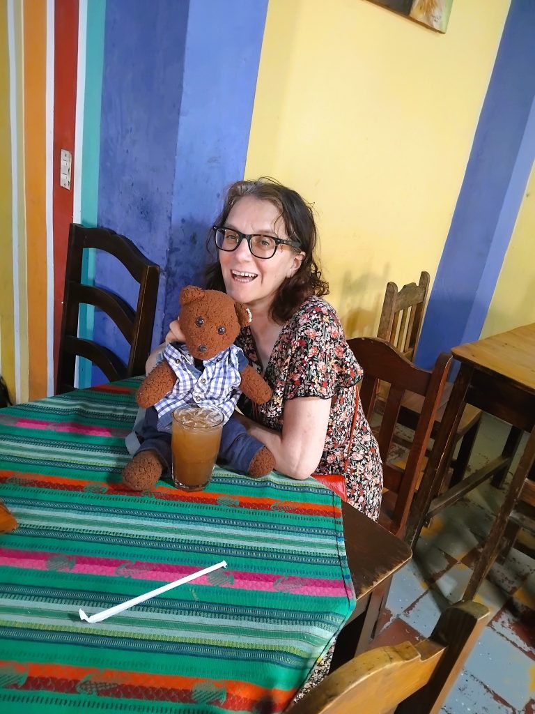 Bearsac the teddy bear iand his human Mummy, Debra sitting a a table with a colourful table cloth.