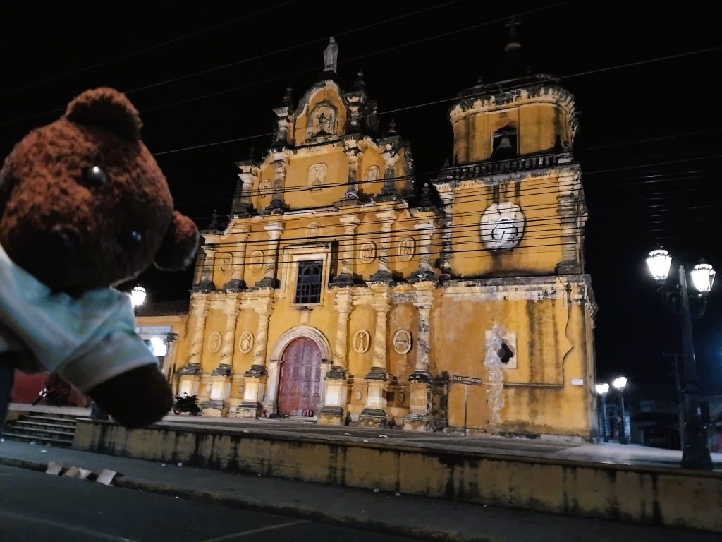 Bearsac the teddy bear in foreground of a church at night.