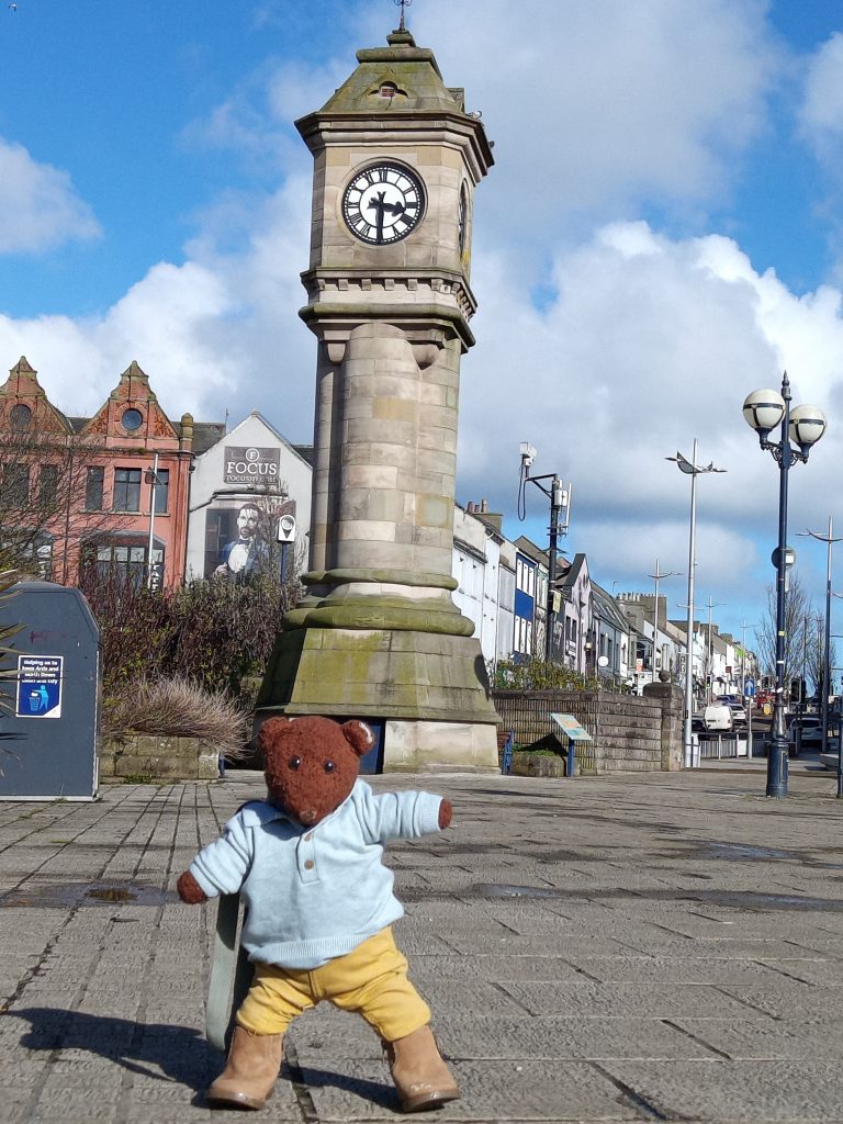 Bearsac the teddy bear in forground of Bangor clock tower