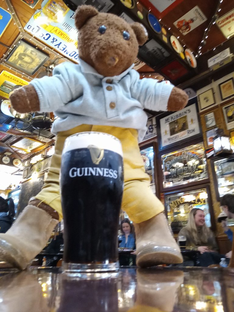 Bearsac the teddy bear standing ona table behind a pint of Guinness