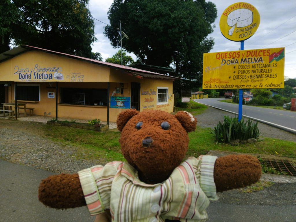 Bearsac the teddy bear in foreground of a cheese and sweets shop.